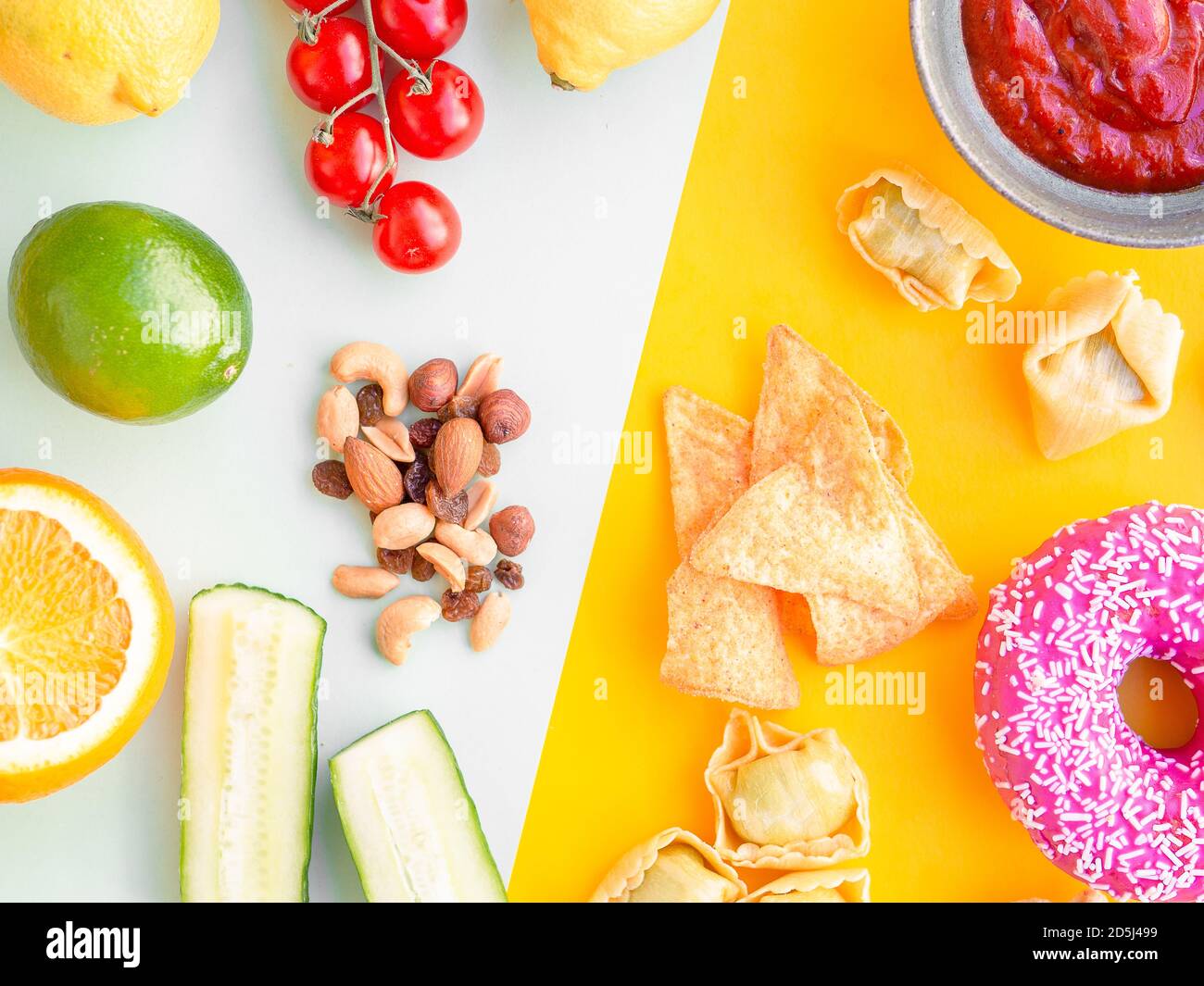 Gesunde und ungesunde Lebensmittel, Diät-Konzept. Fast Food auf gelbem und grünem Gemüse, Nüssen und Früchten auf hellblauem Studiohintergrund mit Kopierraum Stockfoto