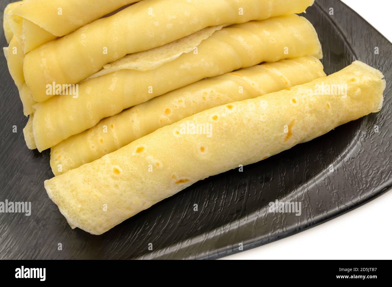 Nahaufnahme eines Stapels gerollter Maida Dosa gefüllt mit Gesüßte geriebene Kokosnuss auf einem schwarzen Teller Stockfoto