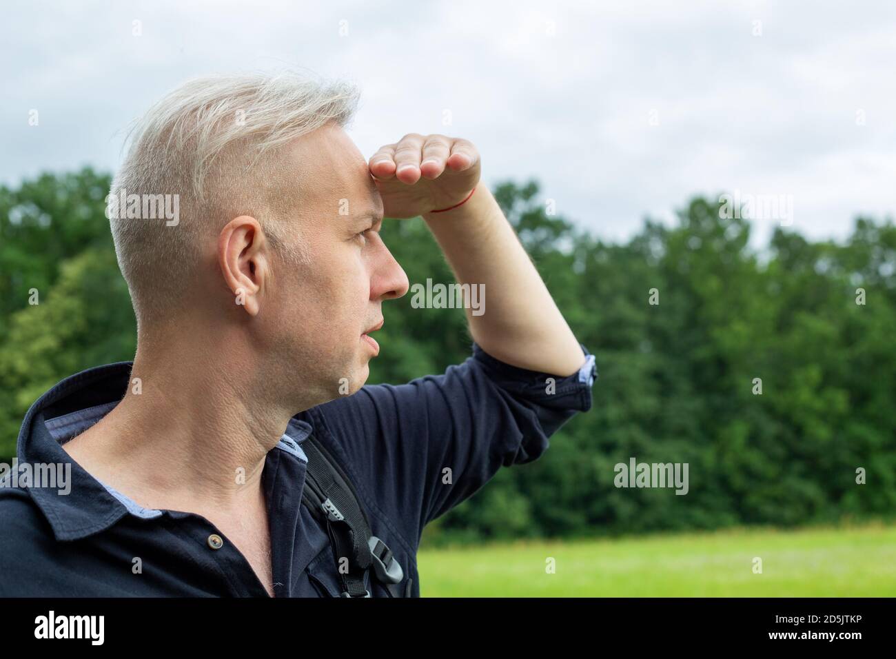Der grauhaarige Mann, der seine Augen mit der Hand vor der Sonne schließt, sieht Stockfoto