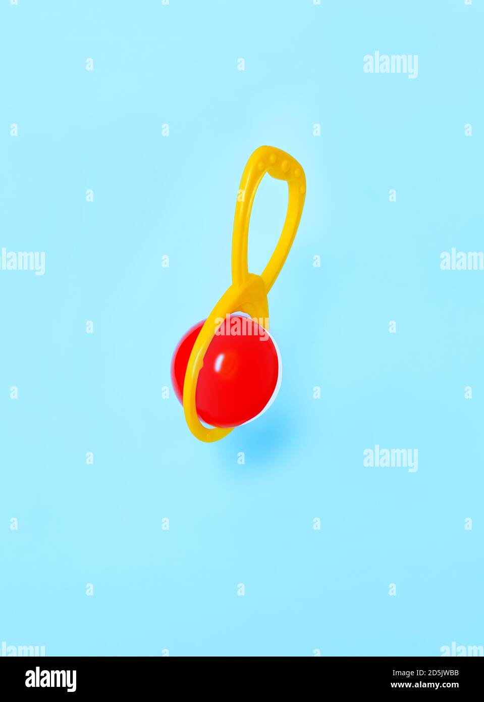 Lustige Karte mit einem Baby Rassel hängen auf blauem Hintergrund. Erstes Sound-Spielzeug für infat Baby. Nahaufnahme der roten und gelben Rassel. Levitationseffekt. Stockfoto