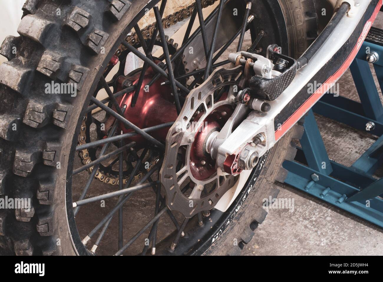 Nahaufnahme Hinterrad mit Nieten eines Enduro Offroad-Motorrads in der Garage auf Lift. Bremsscheiben, Kette, Getriebe. Foto eines Cross-Bike-Teils wurde aufgenommen Stockfoto