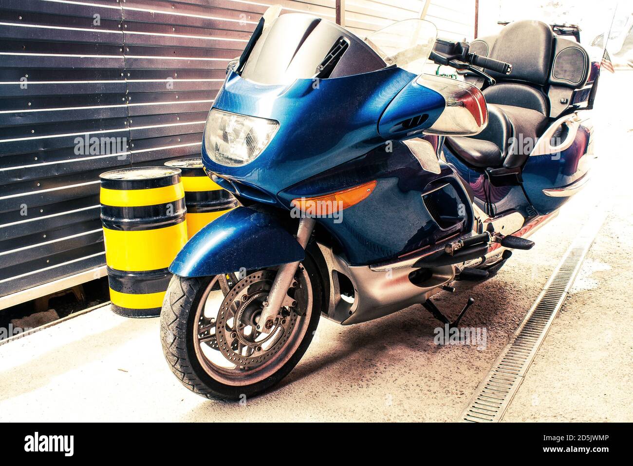Schönes großes blaues Rennrad mit großen Spiegeln in einer Garage mit schwarz-gelben Ölfässern. Kreuzfahrt Motorrad mit bequemen Rücksitz mit Kleiderschrank t Stockfoto