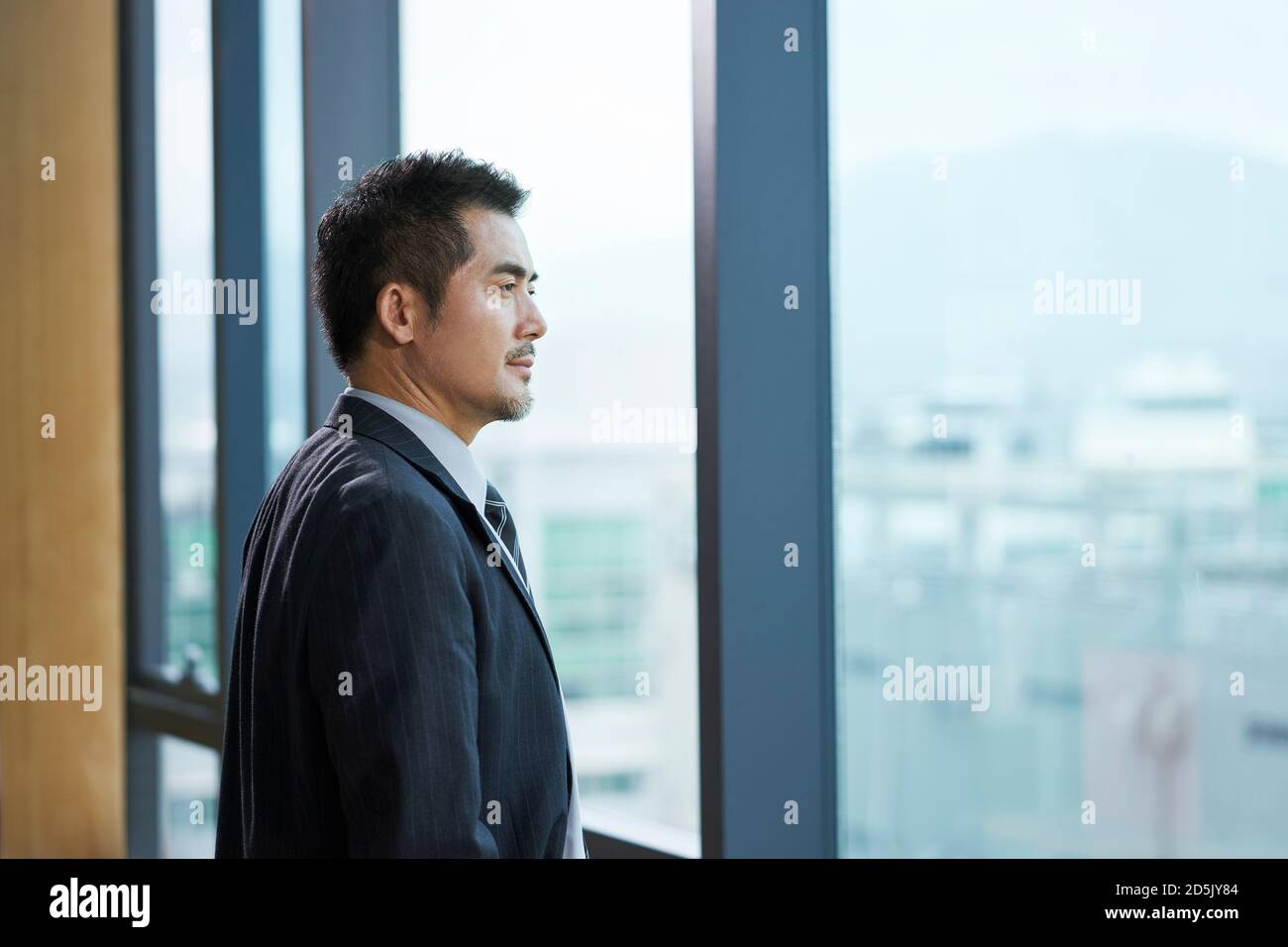der asiatische Geschäftsführer steht am Fenster und blickt hinaus Stockfoto