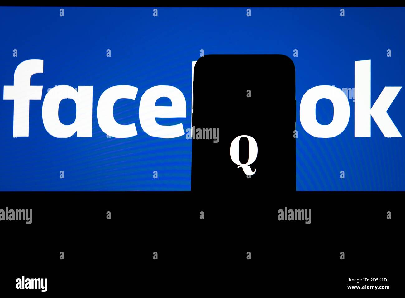 QAnon im Vergleich ZU FACEBOOK. QAnon-Unternehmenslogo auf dem Smartphone, das auf Facebook-Logos platziert ist. Konzept für das Verbot von QAnon in sozialen Medien. Stockfoto