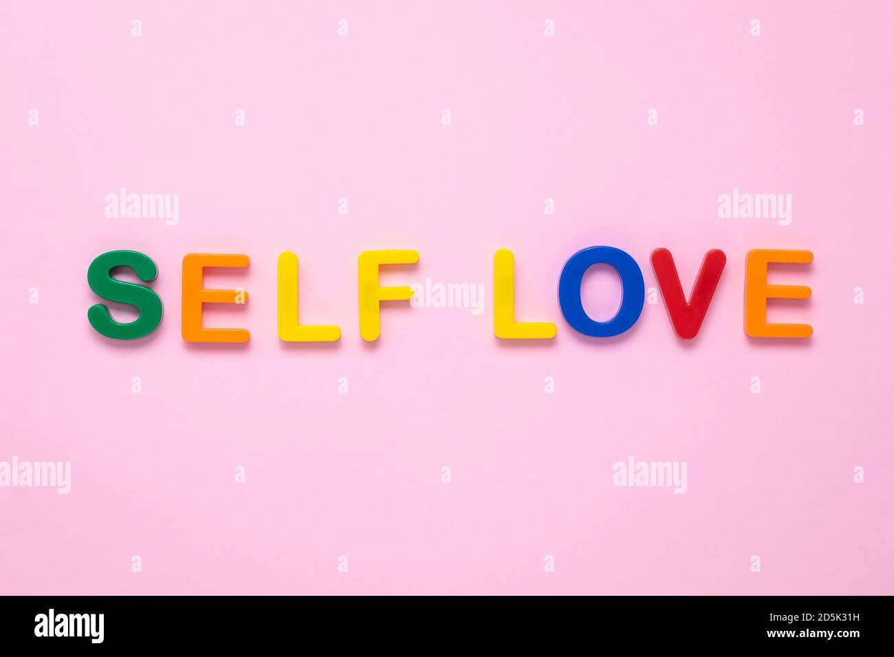 Selbstliebe Text auf rosa Papier Hintergrund aus bunten Kunststoff Buchstaben. Mehrfarbige Inschrift auf dem Banner. Titel, Überschrift. Die Psychologie Co Stockfoto