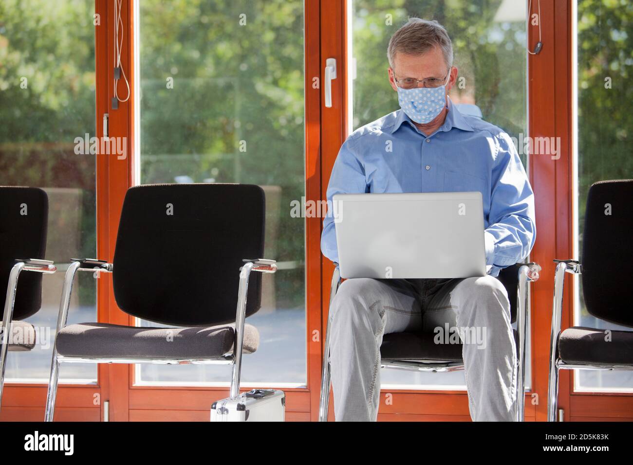 Reife Geschäftsmann mit Gesichtsmaske arbeiten mit Laptop in einem Leerer Warteraum eines Büros oder Krankenhauses - Fokus Auf dem Gesicht Stockfoto