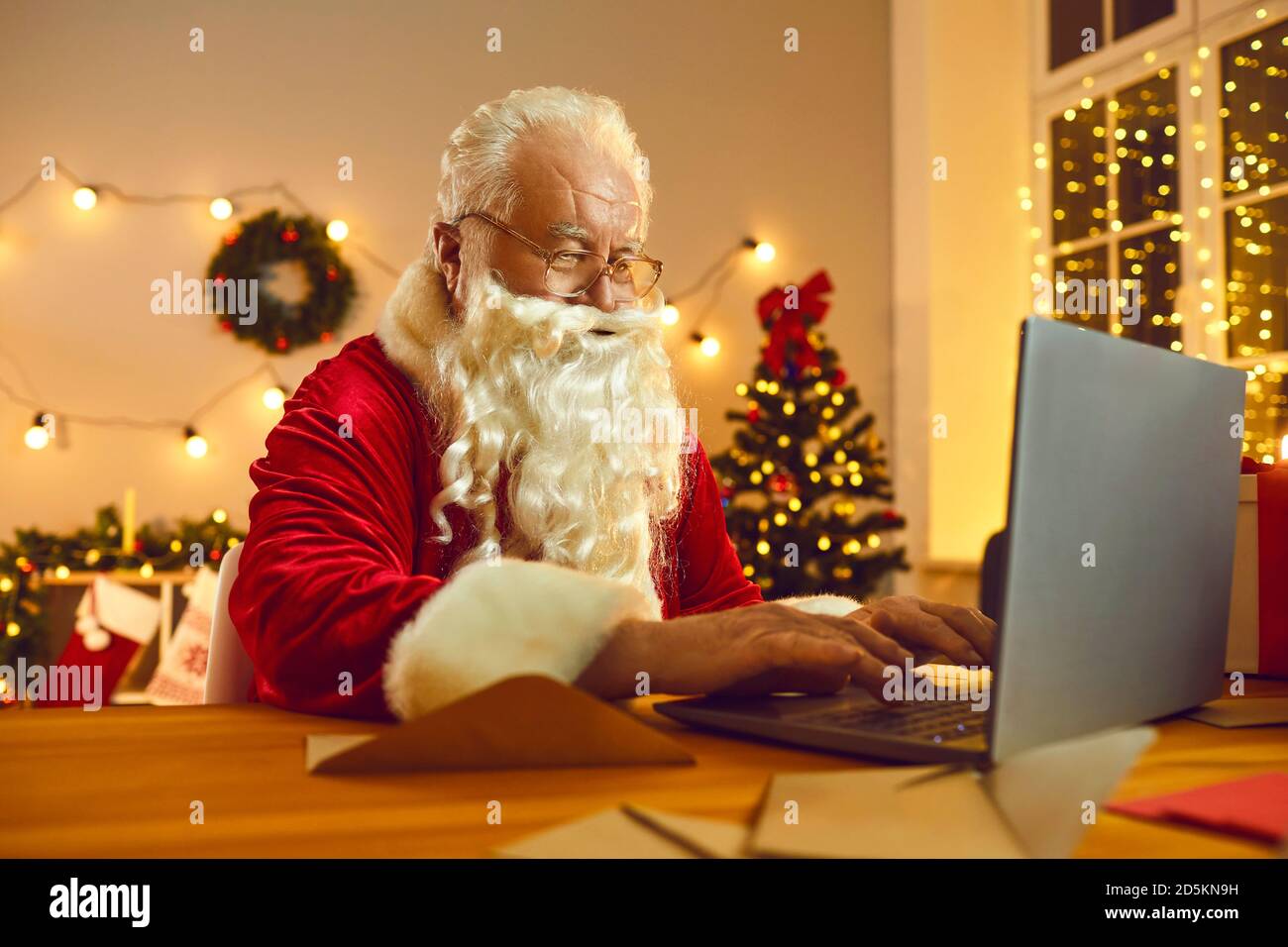 Älterer Weihnachtsmann mit weißem Bart in rotem Kostüm und chatten Herzlichen Glückwunsch online auf Laptop Stockfoto