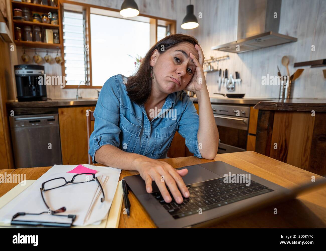 Gestresste Geschäftsfrau, die von zu Hause aus auf einem Laptop arbeitet und besorgt, müde und überfordert aussieht. Erschöpfte Frau, die während der sozialen Distanz fernarbeitet Stockfoto