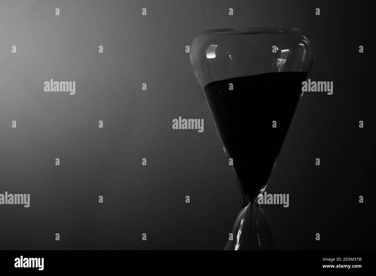 Sanduhr in schwarz & weiß mit dramatischer Beleuchtung auf einem einfachen Hintergrund. Zeit läuft Timer Sand einfachen Hintergrund Stockfoto