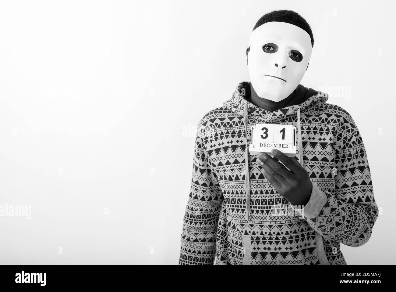 Studioaufnahme eines jungen schwarzen afrikanischen Mannes mit weißer Maske Halten Sie den Kalender für den 31. Dezember ein Stockfoto