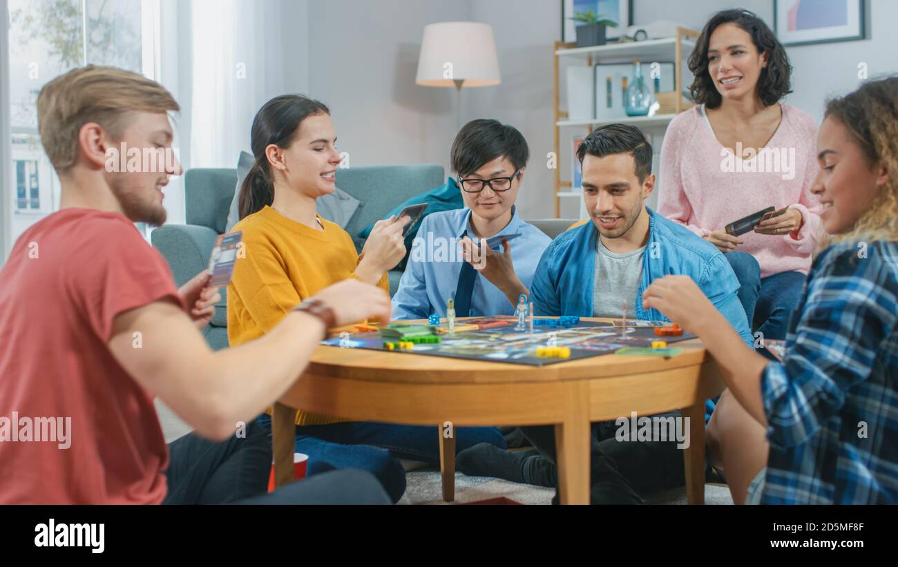 Diverse Gruppe von Jungs und Mädchen spielen in einem strategischen Brettspiel mit Karten und Würfel. Karten lesen und lachen. Freunde, Die Spaß Haben. Gemütliches Wohnen Stockfoto