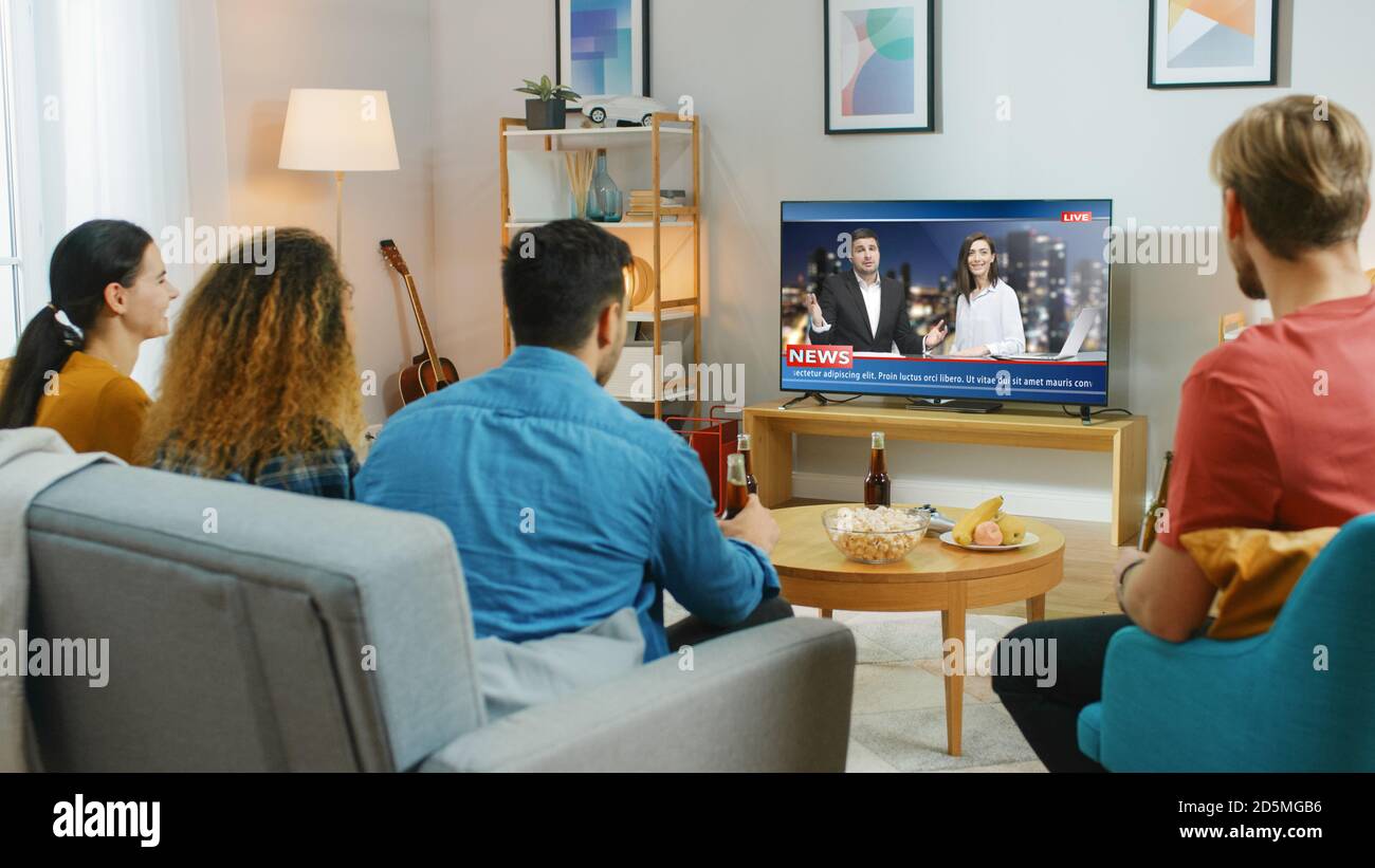 Glückliche Freunde Sitzen Zu Hause Und Schauen Sich Nachrichten An. Entspannen auf einer Couch.Right gemütliche Wohnung mit Freunden essen Snacks und Spaß haben. Stockfoto