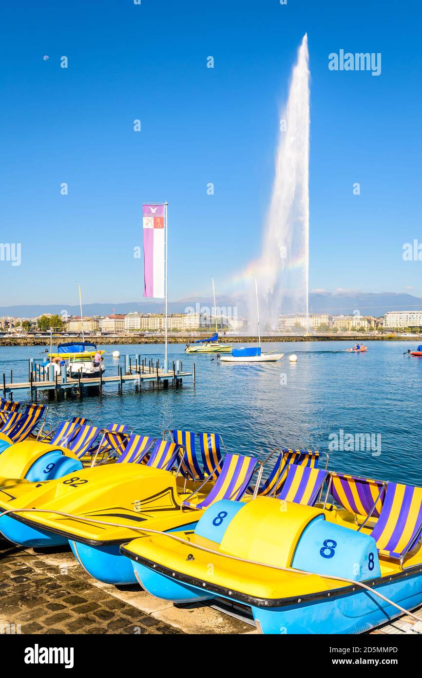 Tretboote Reihen sich an einem sonnigen Sommermorgen am Ufer des Genfer Sees mit dem Jet d'Eau Wasserstrahlbrunnen in der Ferne an. Stockfoto