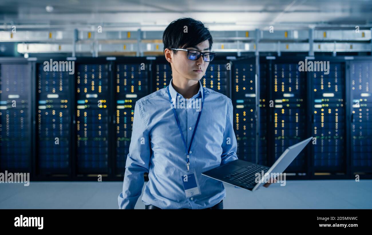 Im modernen Rechenzentrum: Porträt eines IT-Ingenieurs, der mit Server-Racks hinter sich steht, Laptop hält und die Kamera anschaut. Beenden Stockfoto