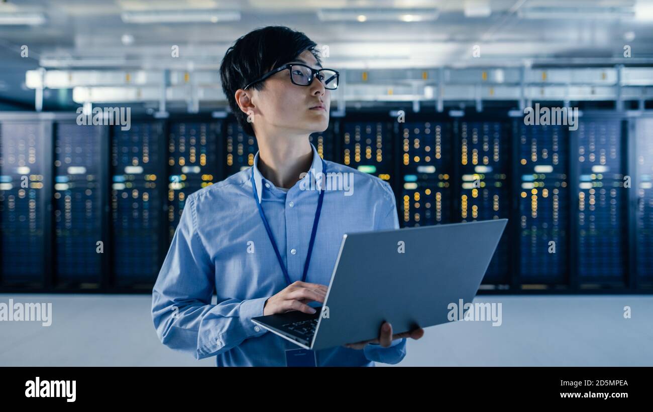 Im modernen Rechenzentrum: Portrait des IT-Ingenieurs Stand in der Nähe von Server-Racks, Finishing Wartung und Diagnose Verfahren Laptop halten. Stockfoto