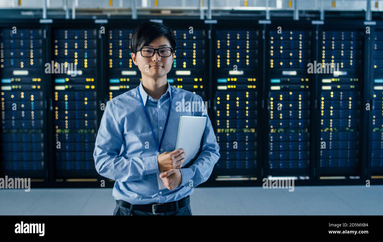 Im modernen Rechenzentrum: Portrait of IT Engineer steht neben der Reihe der Server-Racks, Finishing Maintenance und Diagnostics Procedure und Holding Stockfoto