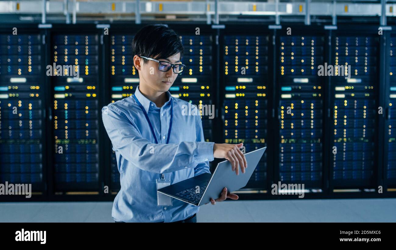 In Dark Data Center: Male IT Specialist steht neben Row of Operational Server Racks, nutzt Laptop für die Wartung. Konzept für Cloud Computing Stockfoto