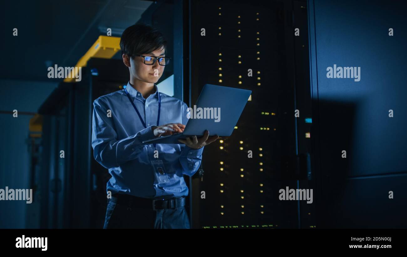 In Dark Data Center: Männlich IT Specialist steht neben der Reihe der operativen Server-Racks, nutzt Laptop für die Wartung. Konzept für Cloud Computing Stockfoto