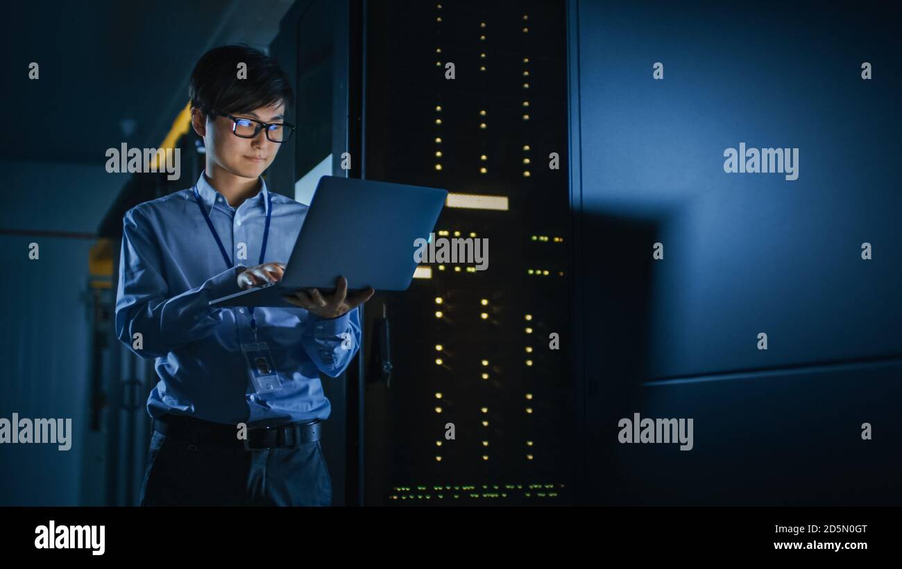 In Dark Data Center: Männlich IT Specialist steht neben der Reihe der operativen Server-Racks, nutzt Laptop für die Wartung. Konzept für Cloud Computing Stockfoto