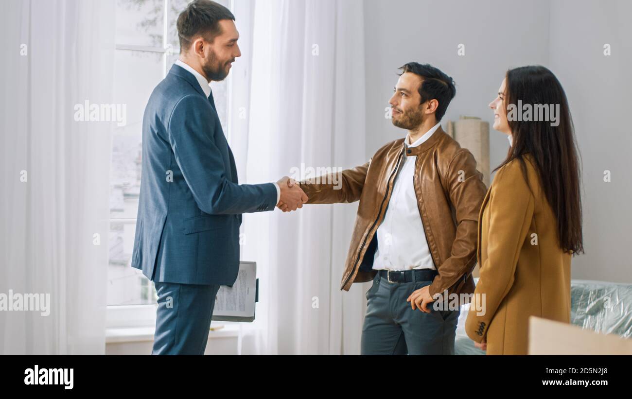 Immobilienmakler zeigt helle neue Wohnung zu einem jungen Paar. Erfolgreiches junges Paar immer Hausbesitzer, Seal the Deal mit Immobilien-Broker durch Stockfoto
