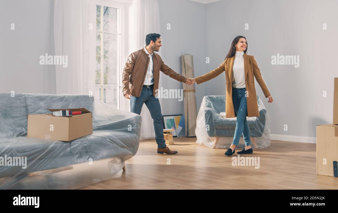 Aufgeregt Junges Paar hält Hände in neu gekauft / Vermietet Wohnung, sie beginnen glücklich Tanzen. Helles modernes Zuhause für glückliche junge Menschen. Stockfoto