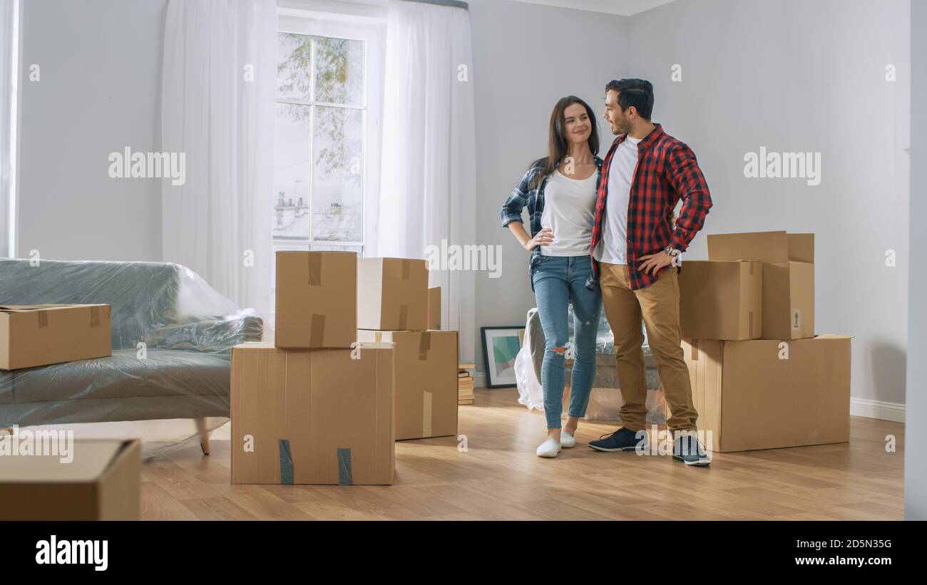 Happy Young Couple Umzug in neue Wohnung, mit Karton-Boxen mit Sachen und Posen auf Kamera. Junge Freund und Freundin Start Living Stockfoto