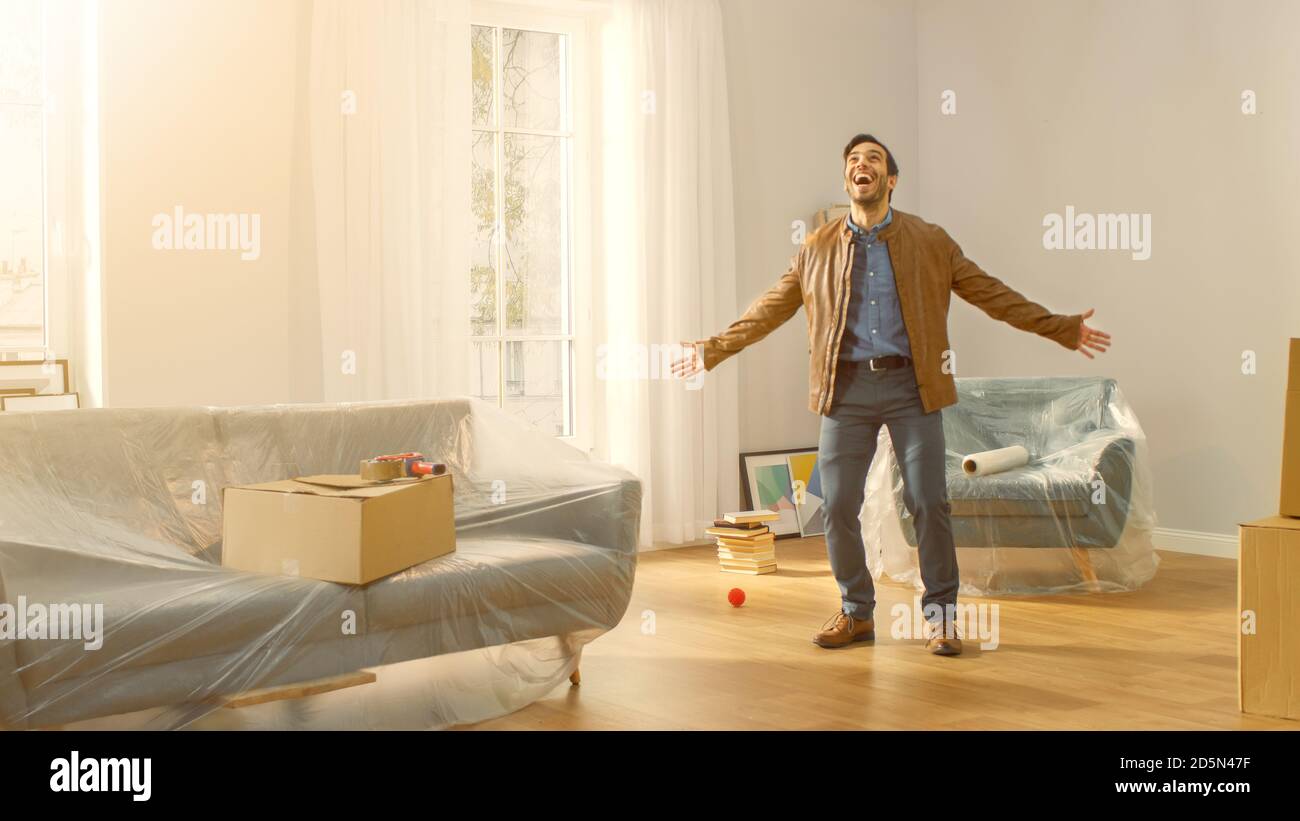 Shot of A Very Happy man zieht in seine neue Wohnung und posiert aufgeregt. Guy kaufte neues Haus bereit zu starten Auspacken Karton-Boxen. Zimmer beleuchtet von Stockfoto