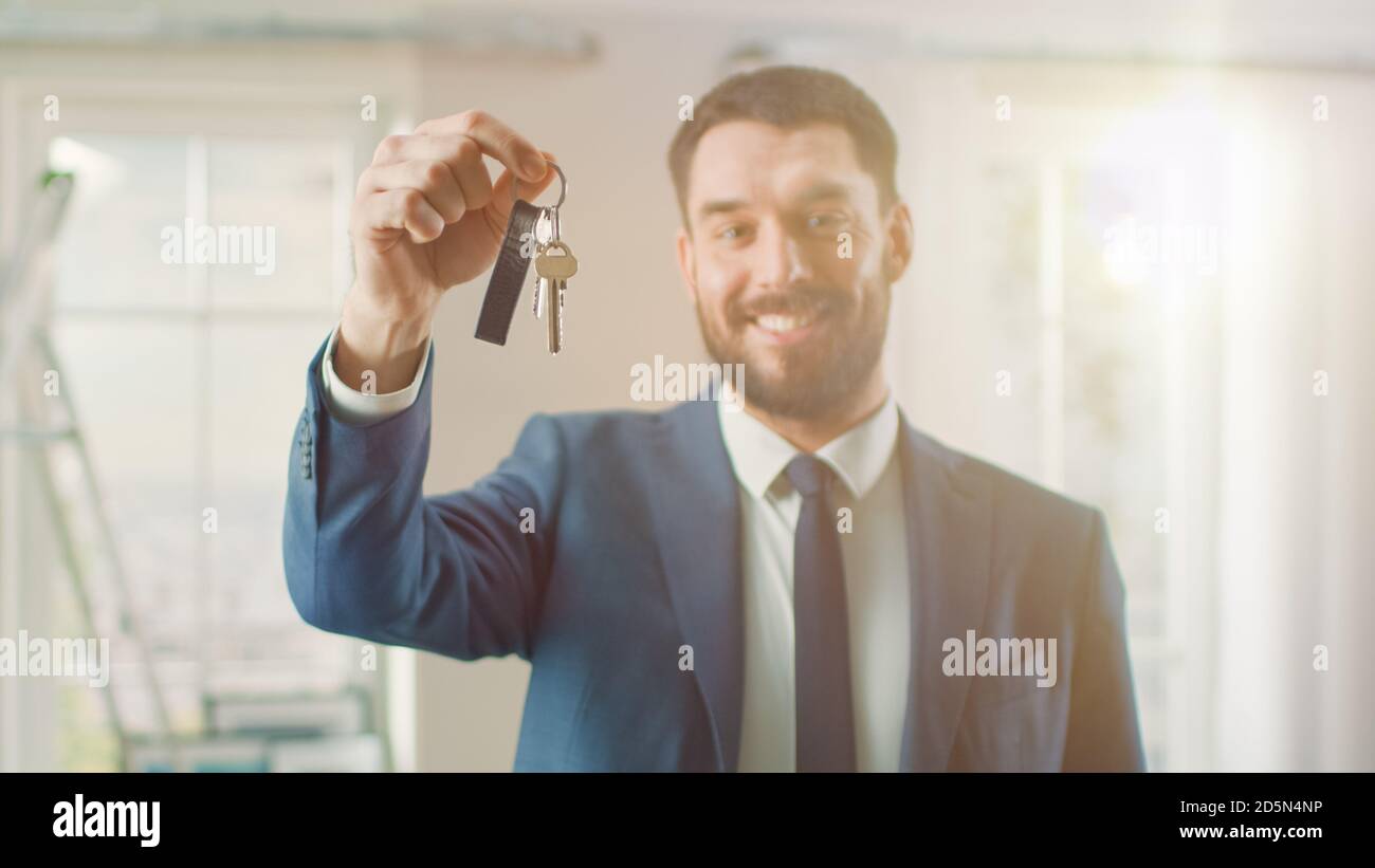 Erfolgreicher Immobilienmakler in einem Anzug smiles und bietet Schlüssel aus einer neuen Wohnung. Geräumiges neues Haus zum Verkauf von professionellen Immobilienmaklern Stockfoto