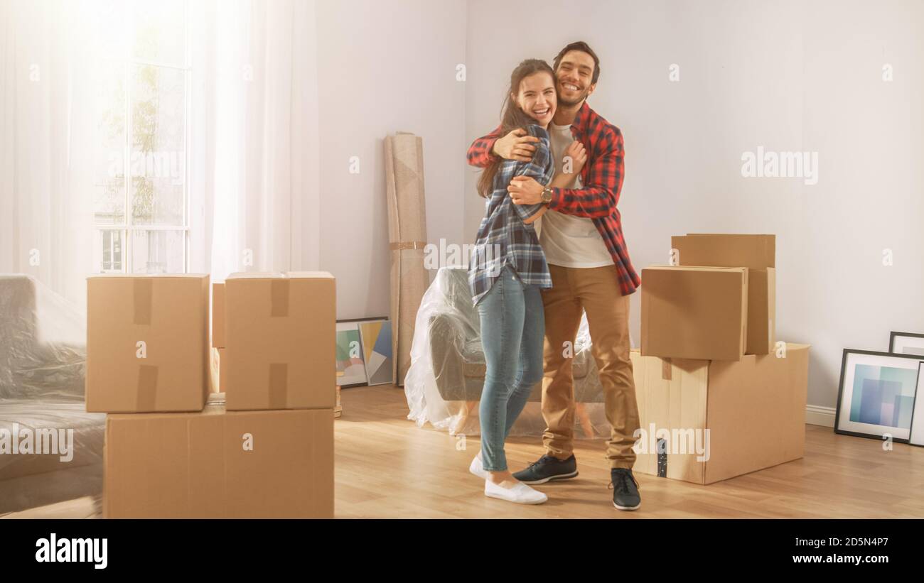 Junges Paar zieht in neue Wohnung, mit Karton-Boxen mit Sachen, mit Spaß und Umarmung. Freund und Freundin beginnen zusammen zu leben Stockfoto