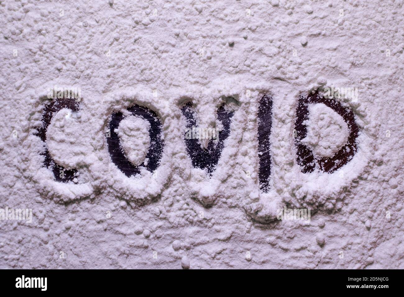 Covid Text in weißem Pulver, Mehl geschrieben. Konzepte der covid Pandemie, die die Backindustrie betrifft. Weiße Substanz könnte als Kokain, Droge ab gesehen werden Stockfoto