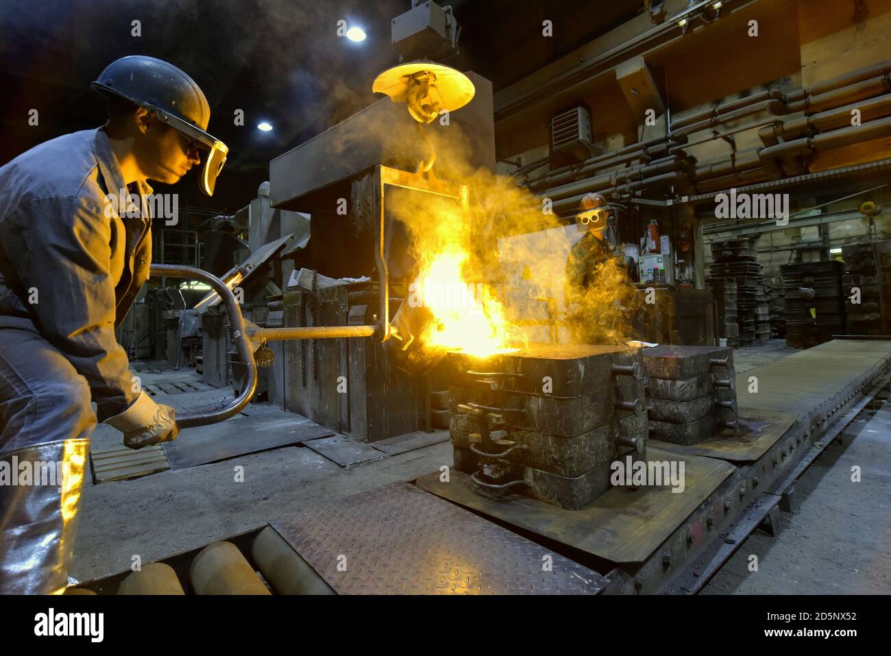 Arbeitnehmer in einer Gießerei gießen ein Werkstück aus Metall - Sicherheit bei der Arbeit und Teamarbeit Stockfoto