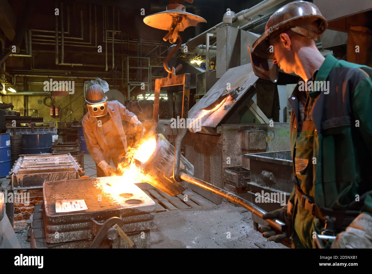 Arbeitnehmer in einer Gießerei gießen ein Werkstück aus Metall - Sicherheit bei der Arbeit und Teamarbeit Stockfoto