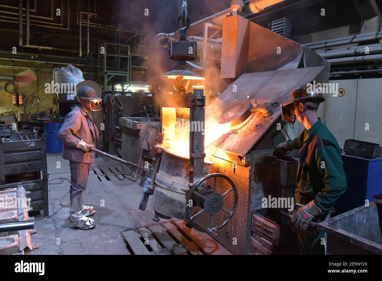 Arbeitnehmer in einer Gießerei gießen ein Werkstück aus Metall - Sicherheit bei der Arbeit und Teamarbeit Stockfoto