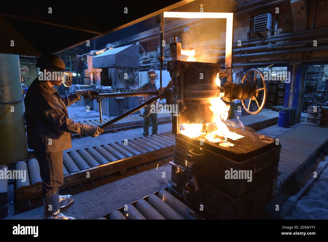 Arbeitnehmer in einer Gießerei gießen ein Werkstück aus Metall - Sicherheit bei der Arbeit und Teamarbeit Stockfoto