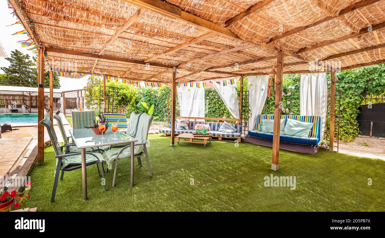 Außenpanorama eines Pavillons in einem Loungebereich in einer entspannenden Ferienvilla mit Sofas, Kissen, Tisch, Stühlen, Gras und Garten Stockfoto