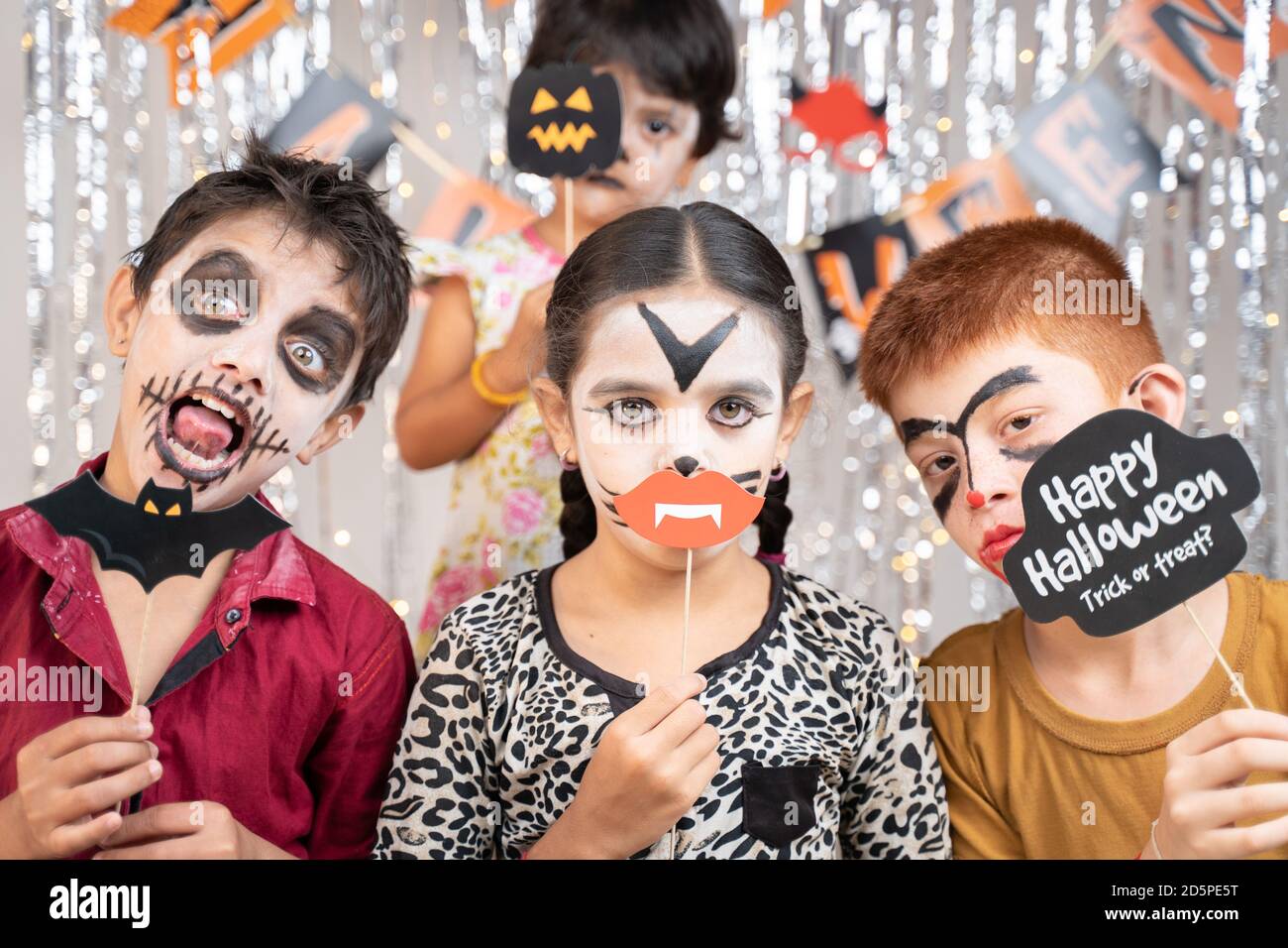 Gruppe von Kindern in Halloween-Kostümen machen gestikulierend beängstigend oder gruselige Gesichter, indem sie Stand Sprops auf dekorierten Hintergrund halten, indem sie in die Kamera schauen. Stockfoto