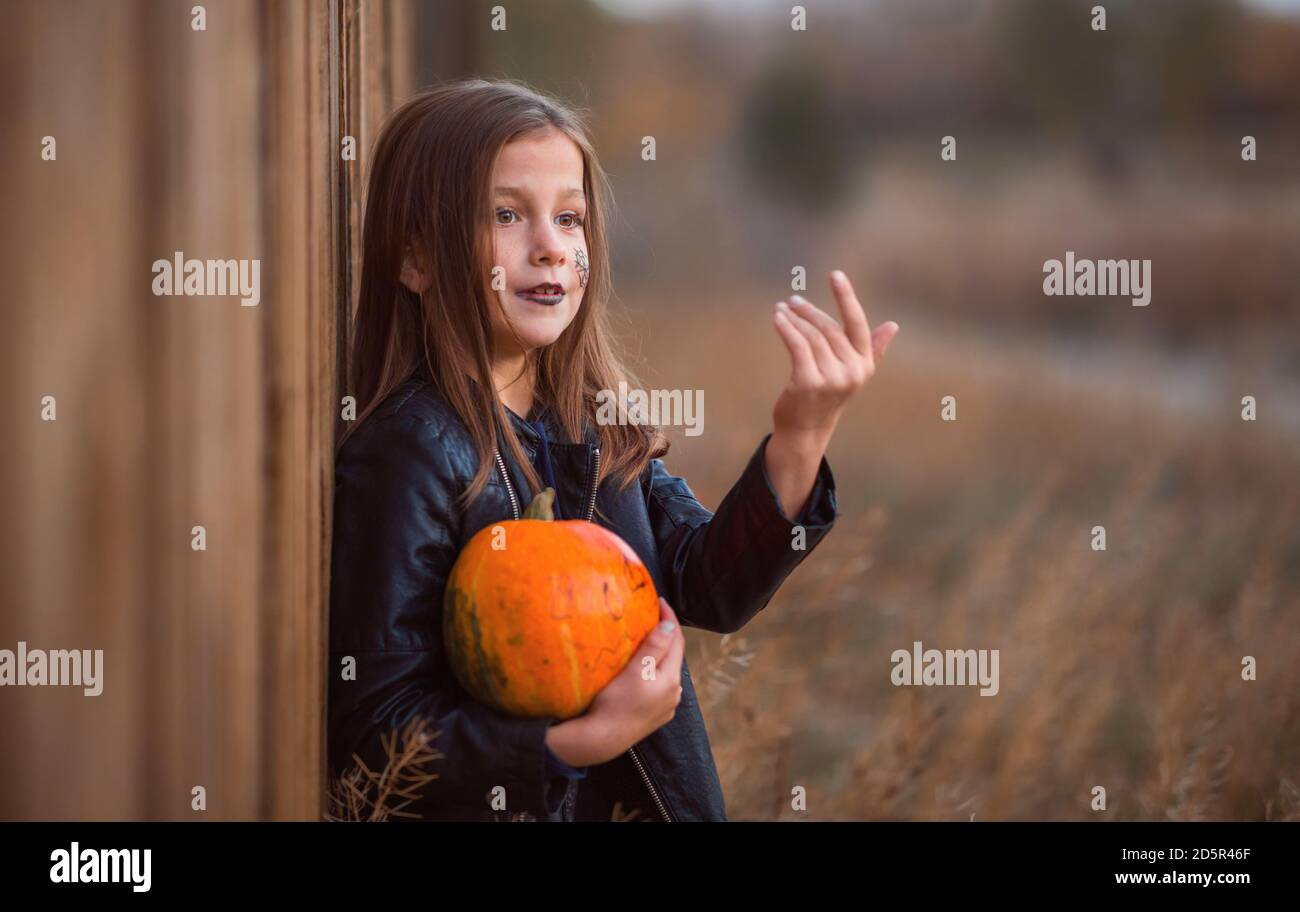 Porträt eines Teenagers in dunkler Kleidung auf einem hölzernen Hintergrund mit einem orangefarbenen Kürbis. Stockfoto