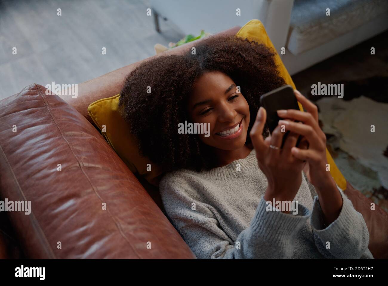 Hochwinkel-Porträt-Ansicht der fröhlichen afrikanischen Frau liegend auf Couch mit Smartphone zu Hause Stockfoto