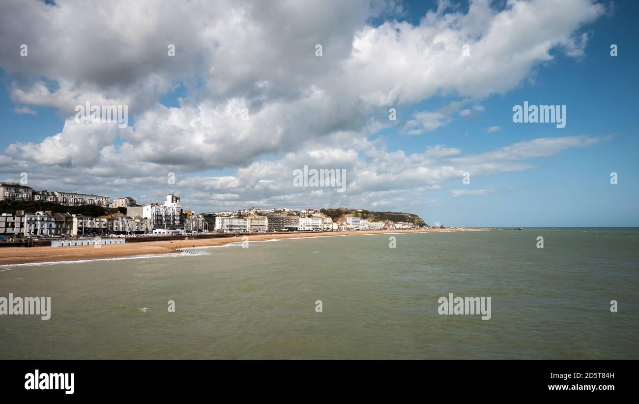 Hastings, East Sussex, England. Die Strandpromenade zum Küstenort an der britischen Südküste mit seinem Wahrzeichen Burg sichtbar auf dem Hügel. Stockfoto