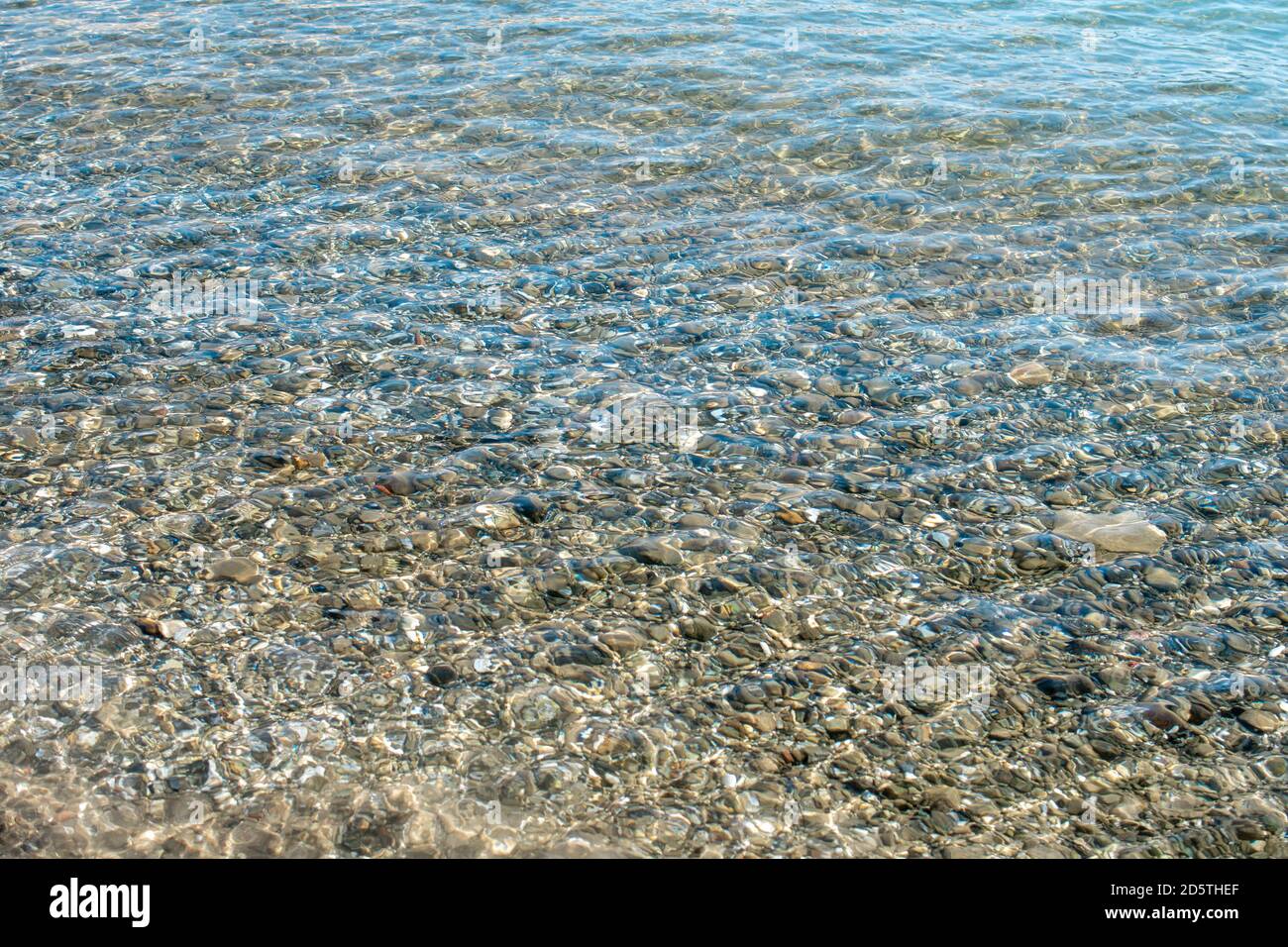 Klares Wasser und Steine. Farbige Kieselsteine unter klarem Meerwasser. Transparentes Wasser in flachen Gewässern auf See. Sauberes Wasser im Meer. Naturkonzept mit Stockfoto
