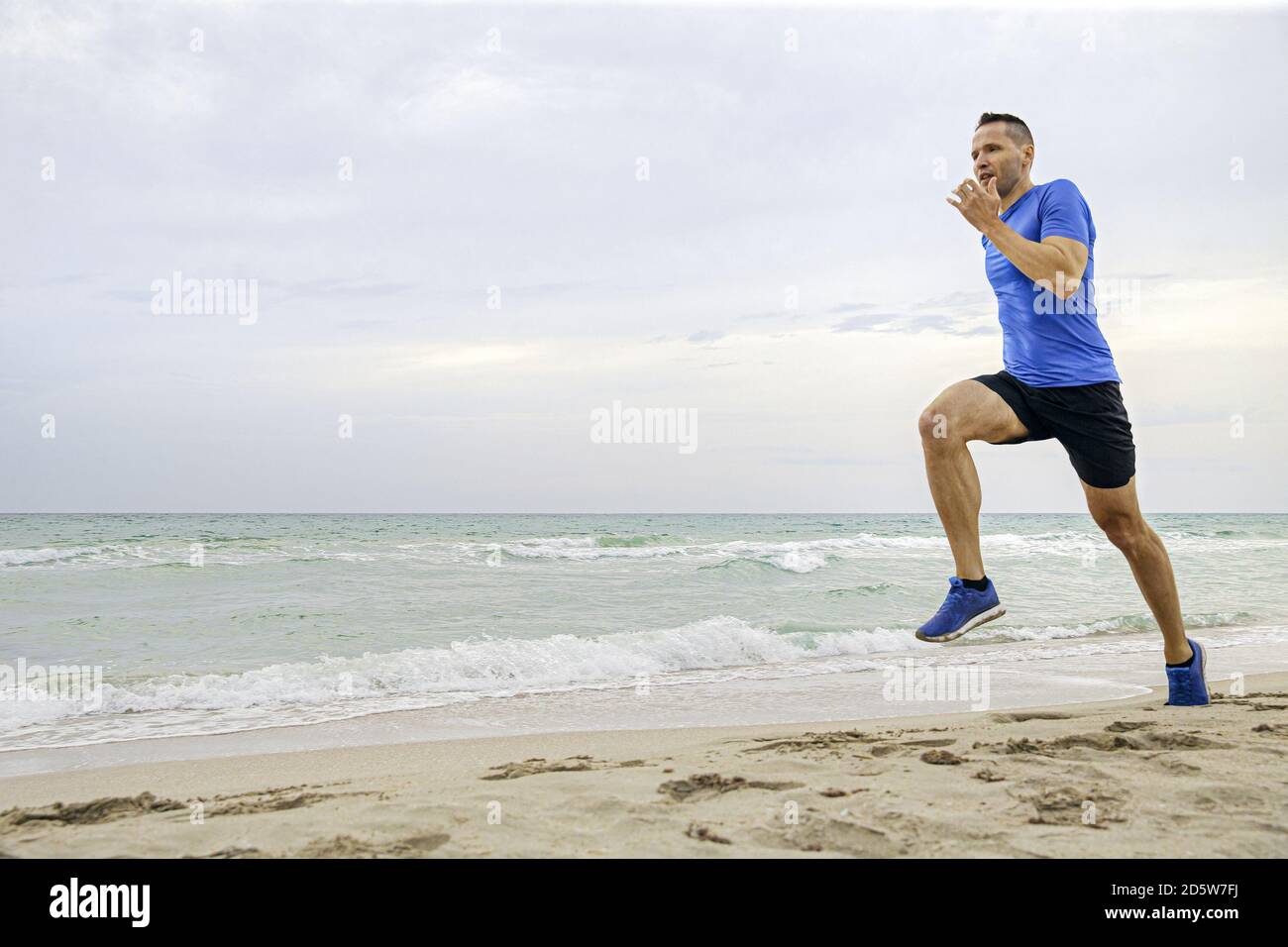 Mann Läufer mittleren Alters laufen auf Sandstrand des Meeres Stockfoto
