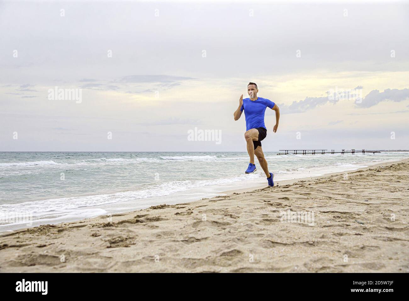 Männlicher Läufer, der ein Abendtraining am Sandstrand ausführt Stockfoto