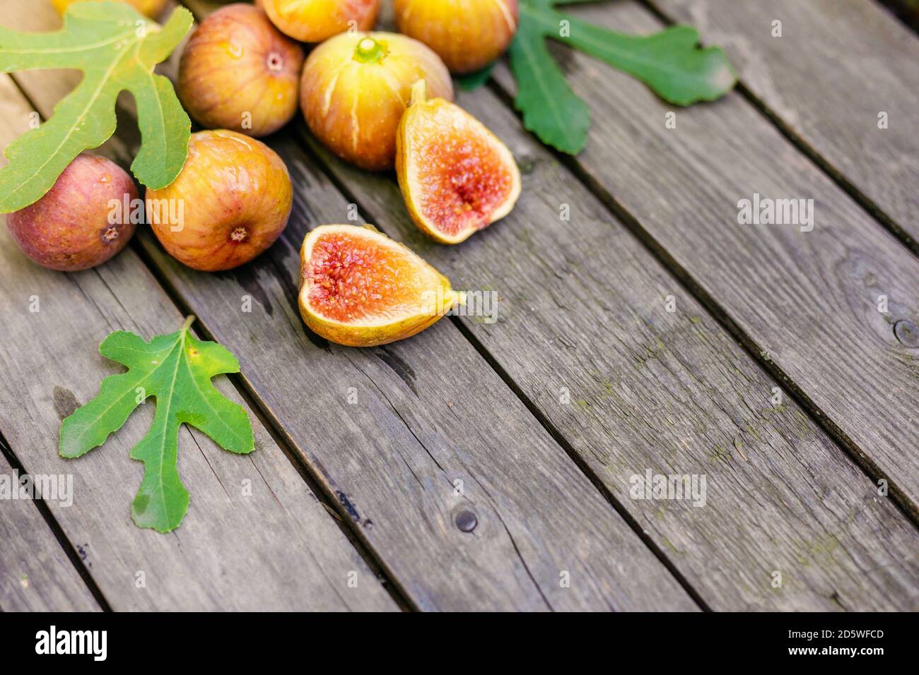 Frische Feigen in zwei Hälften geschnitten mit ganzen Feigen im Hintergrund, auf einer hölzernen Oberfläche. Feigen Sie die Früchte auf einer hölzernen Platte Stockfoto