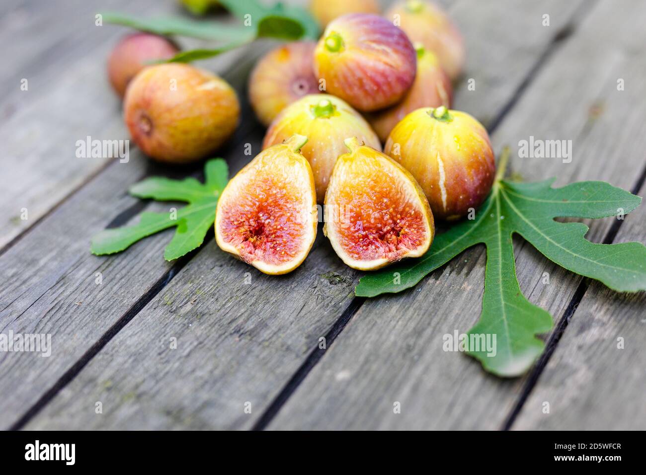 Frische Feigen in zwei Hälften geschnitten mit ganzen Feigen im Hintergrund, auf einer hölzernen Oberfläche. Feigen Sie die Früchte auf einer hölzernen Platte Stockfoto