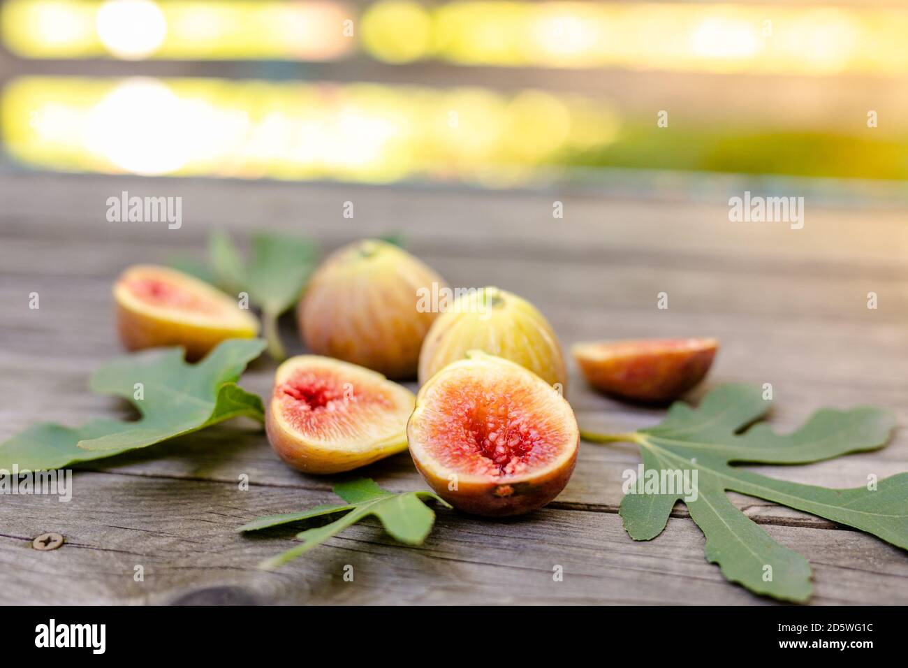 Frische Feigen in zwei Hälften geschnitten mit ganzen Feigen im Hintergrund, auf einer hölzernen Oberfläche. Feigen Sie die Früchte auf einer hölzernen Platte Stockfoto