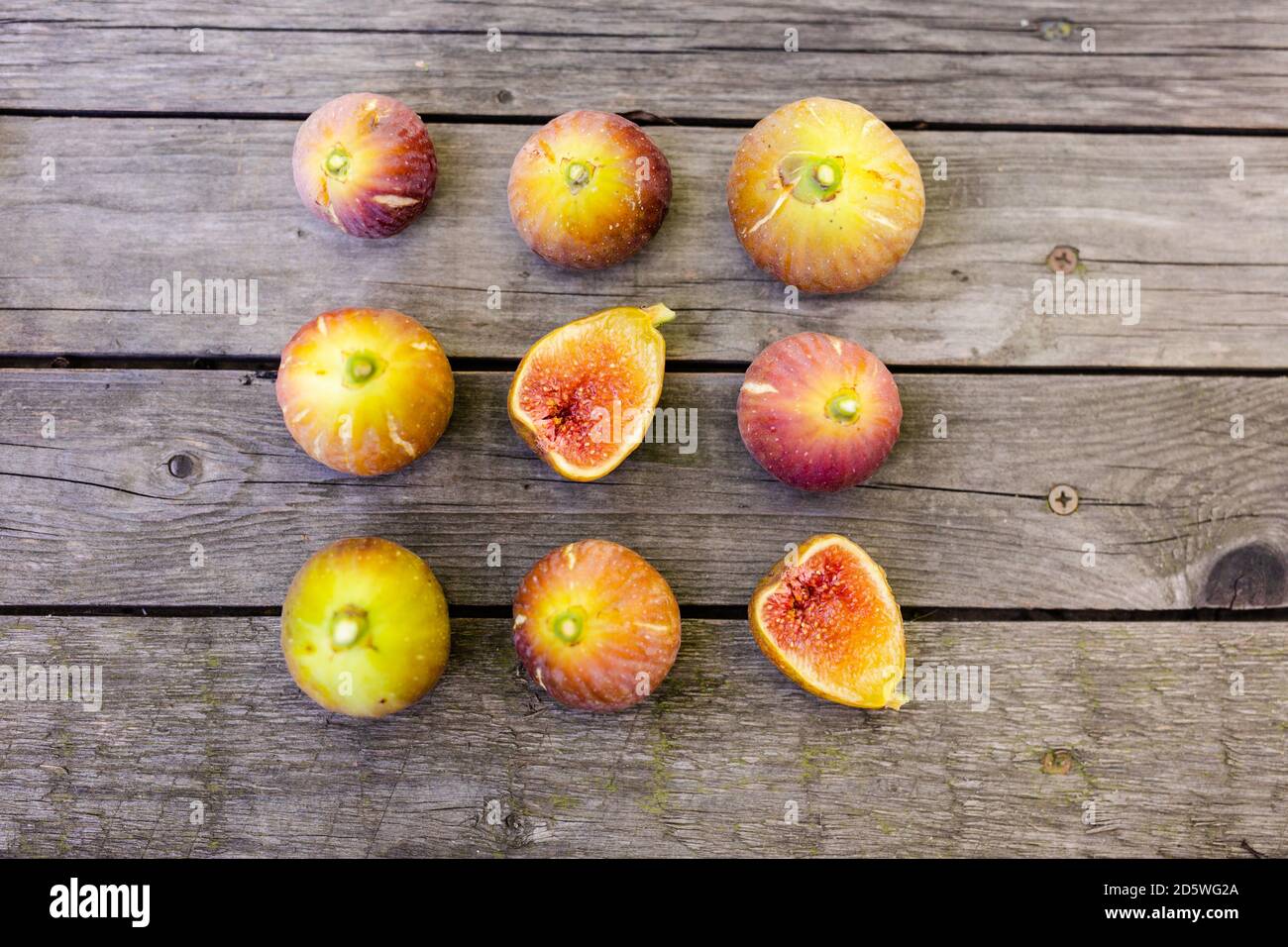 Frische Feigen in zwei Hälften geschnitten mit ganzen Feigen im Hintergrund, auf einer hölzernen Oberfläche. Feigen Sie die Früchte auf einer hölzernen Platte Stockfoto