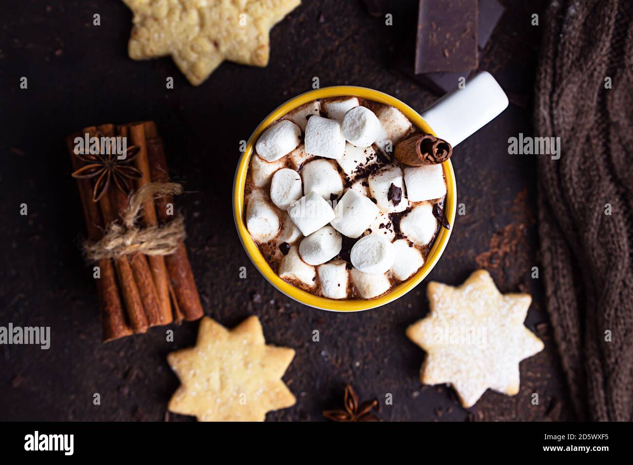 Zwei weiße Keramikbecher mit heißem Kakao oder Schokolade mit Marshmallow und Anis, Zimt und Bitterschokolade auf dunkelbraunem Steingrund. Stockfoto