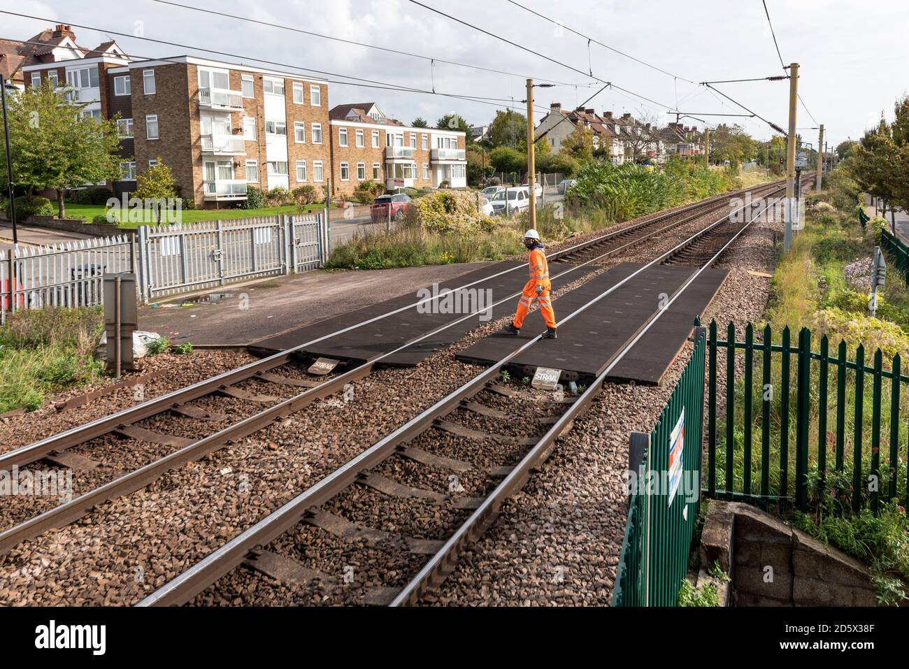 Bahnarbeiter, der über eine Kreuzung auf der C2C Fenchurch Street zur Southend Line in Westcliff on Sea, Essex, Großbritannien, geht. Schwarz männlich, Person der Farbe Stockfoto