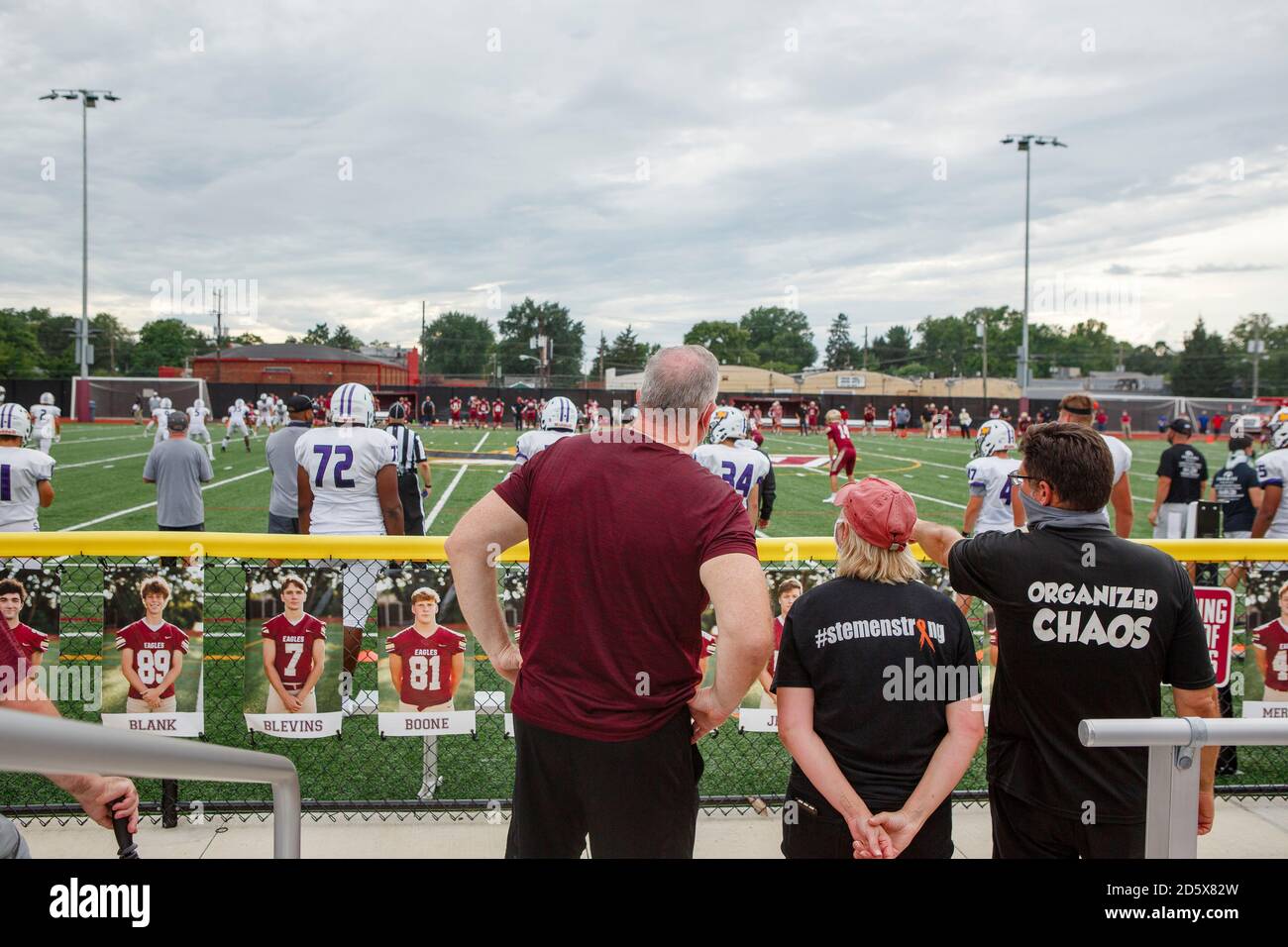 Drei Zuschauer stehen am Zaun und beobachten einen High-School-Fußball Spiel Stockfoto