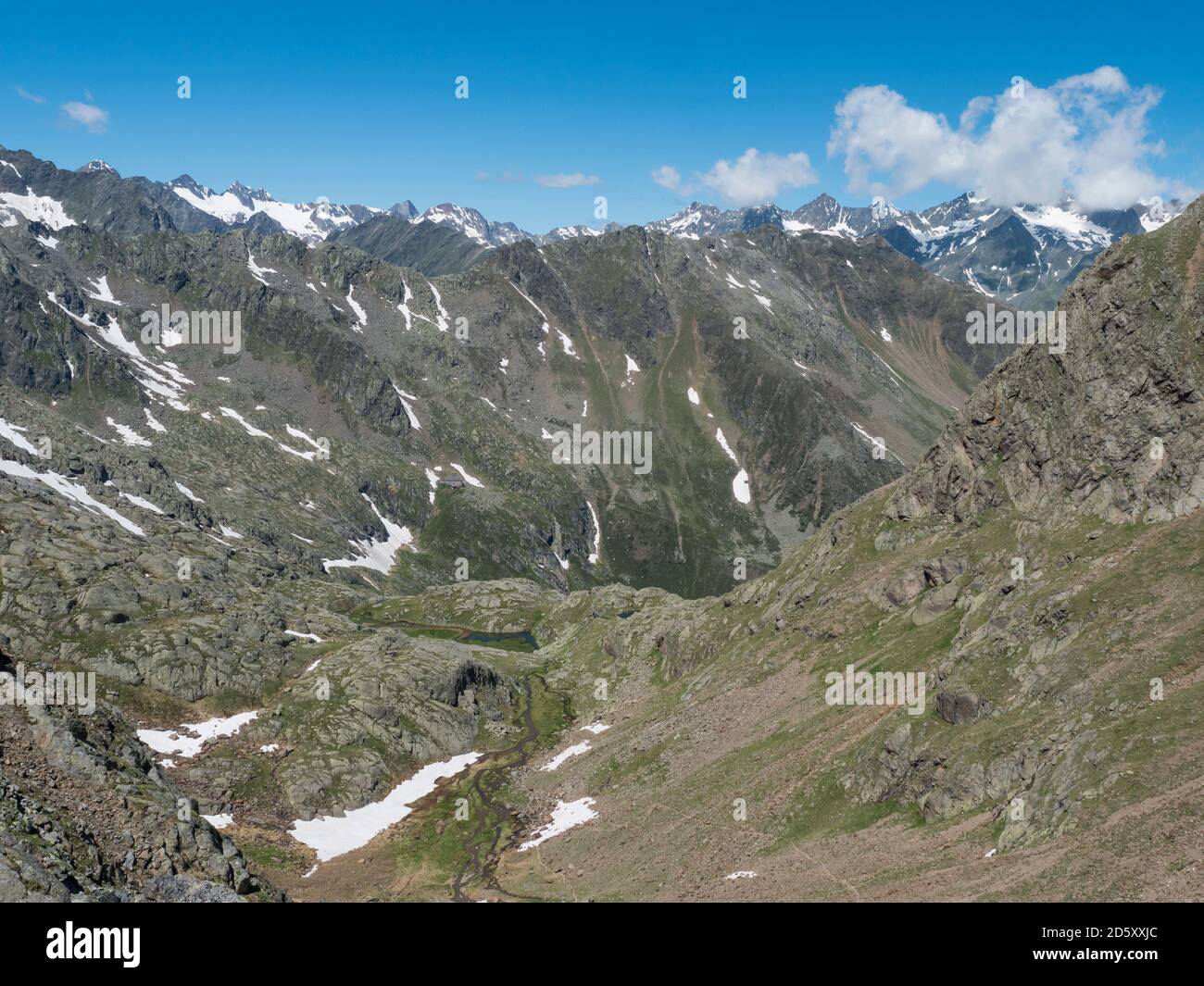 Blick auf das Bergtal mit gewundenem Quellbach und schneebedeckten Gipfeln am Stubaier Wanderweg, Stubaier Hohenweg, Sommer felsige Alpenlandschaft Stockfoto